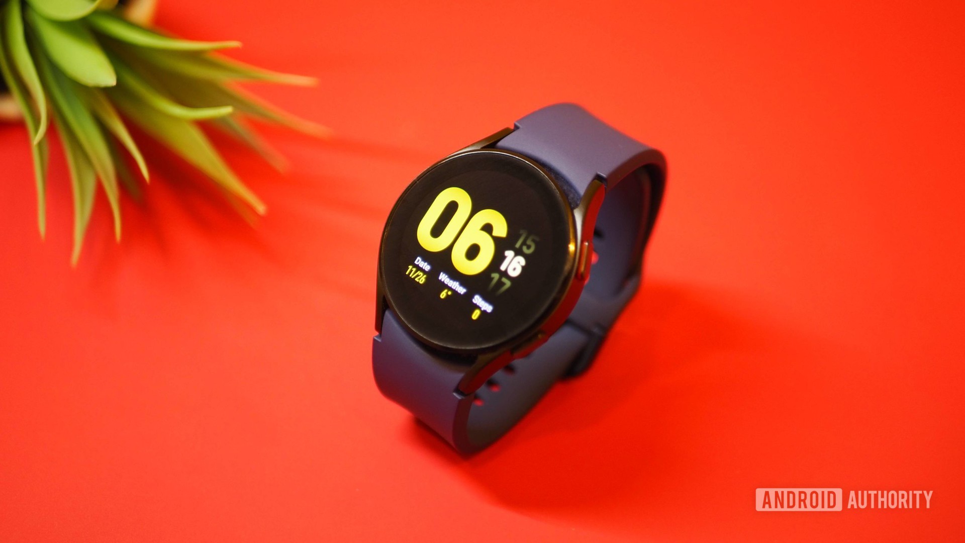 Samsung Galaxy Watch 4 em fundo vermelho, mostrando o relógio da tela inicial
