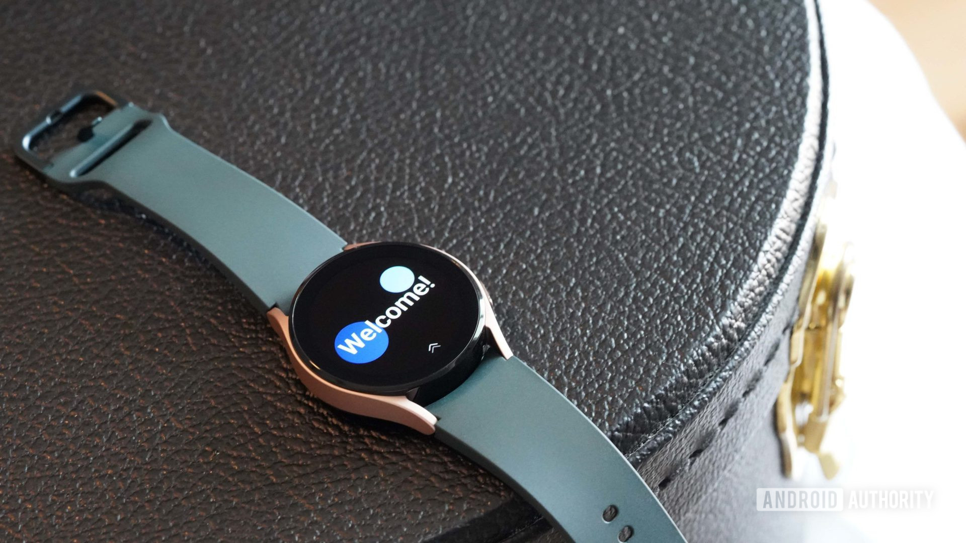 Um Samsung Galaxy Watch 4 repousa sobre um estojo de couro preto exibindo a tela de boas-vindas do relógio.