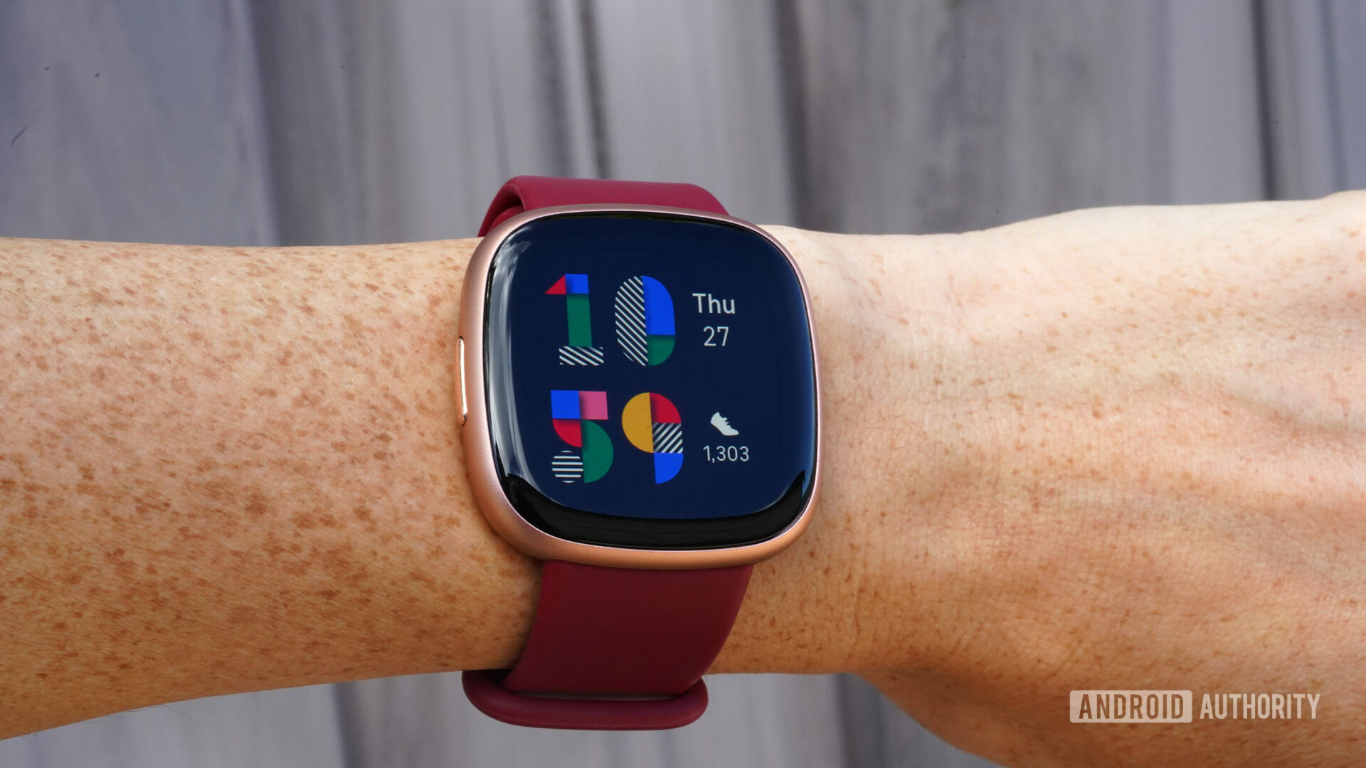 Fitbit Versa 4 Playpen Face Um Fitbit Versa 4 no pulso de um usuário exibe o rosto colorido do Playpen Watch.