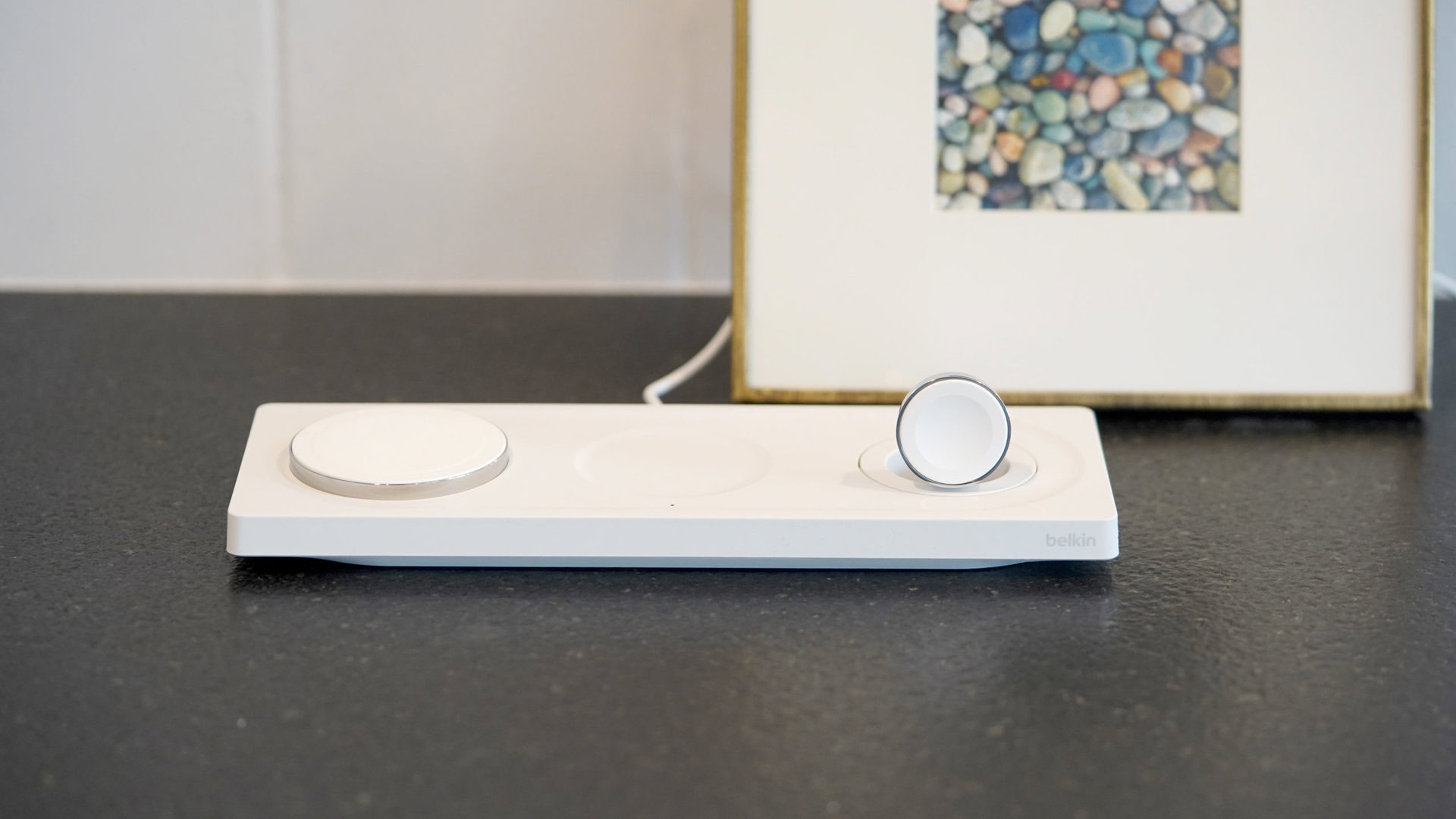 Uma almofada de carregamento sem fio Belkin BoostCharge Pro 3 em 1 repousa em uma bancada preta.