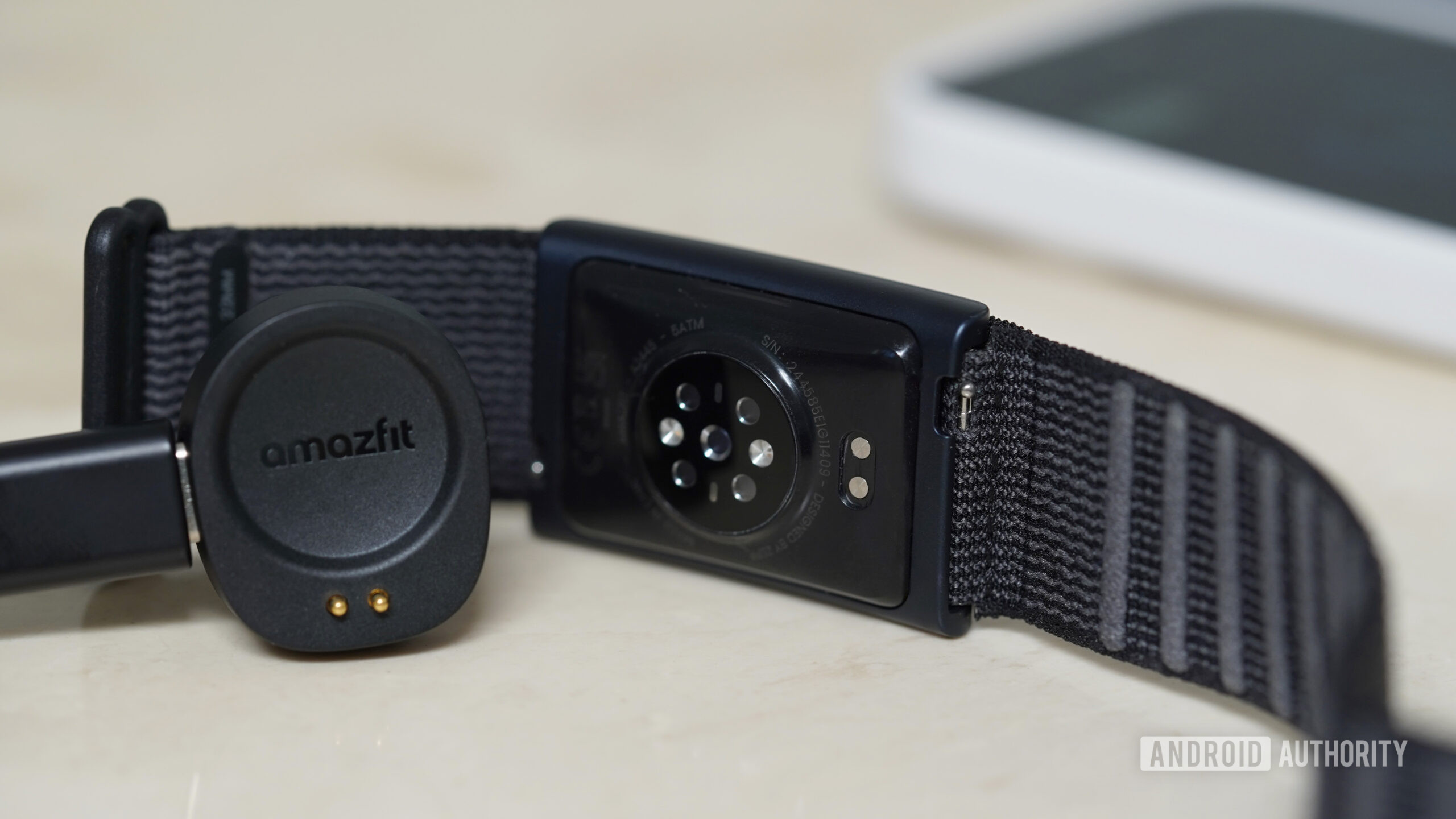 Uma correia do Amazfit Helio repousa ao lado de seu carregador.