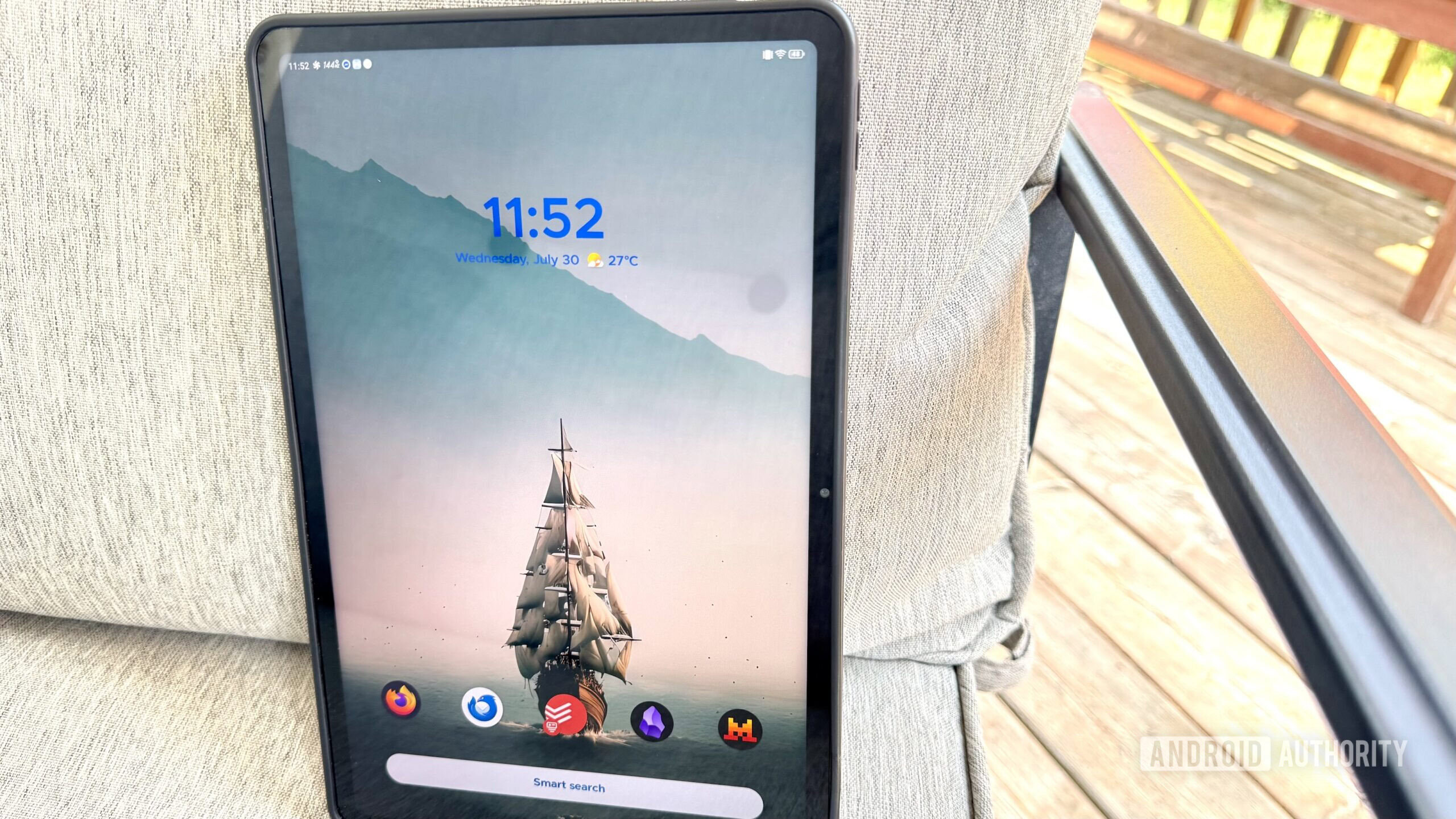 Cadeira de tablets do lançador SMART 6 Um tablet Redmagic Nova em uma cadeira cinza com um pátio de madeira ao fundo.