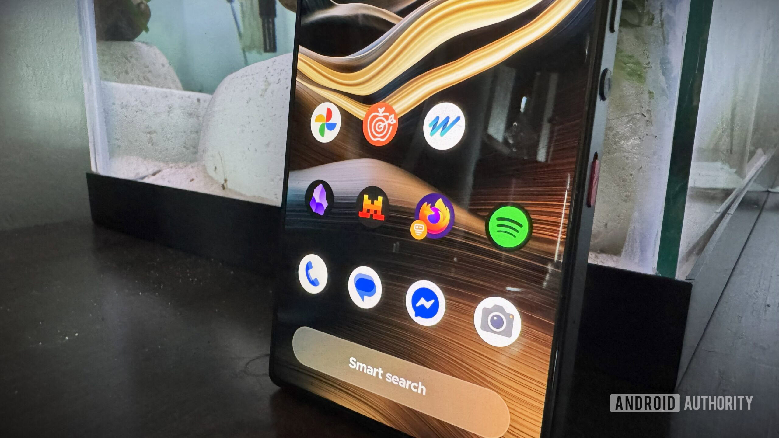 Aqui vamos nós, ícone, Android Um telefone Android encostado a um aquário com vários aplicativos na tela inicial.