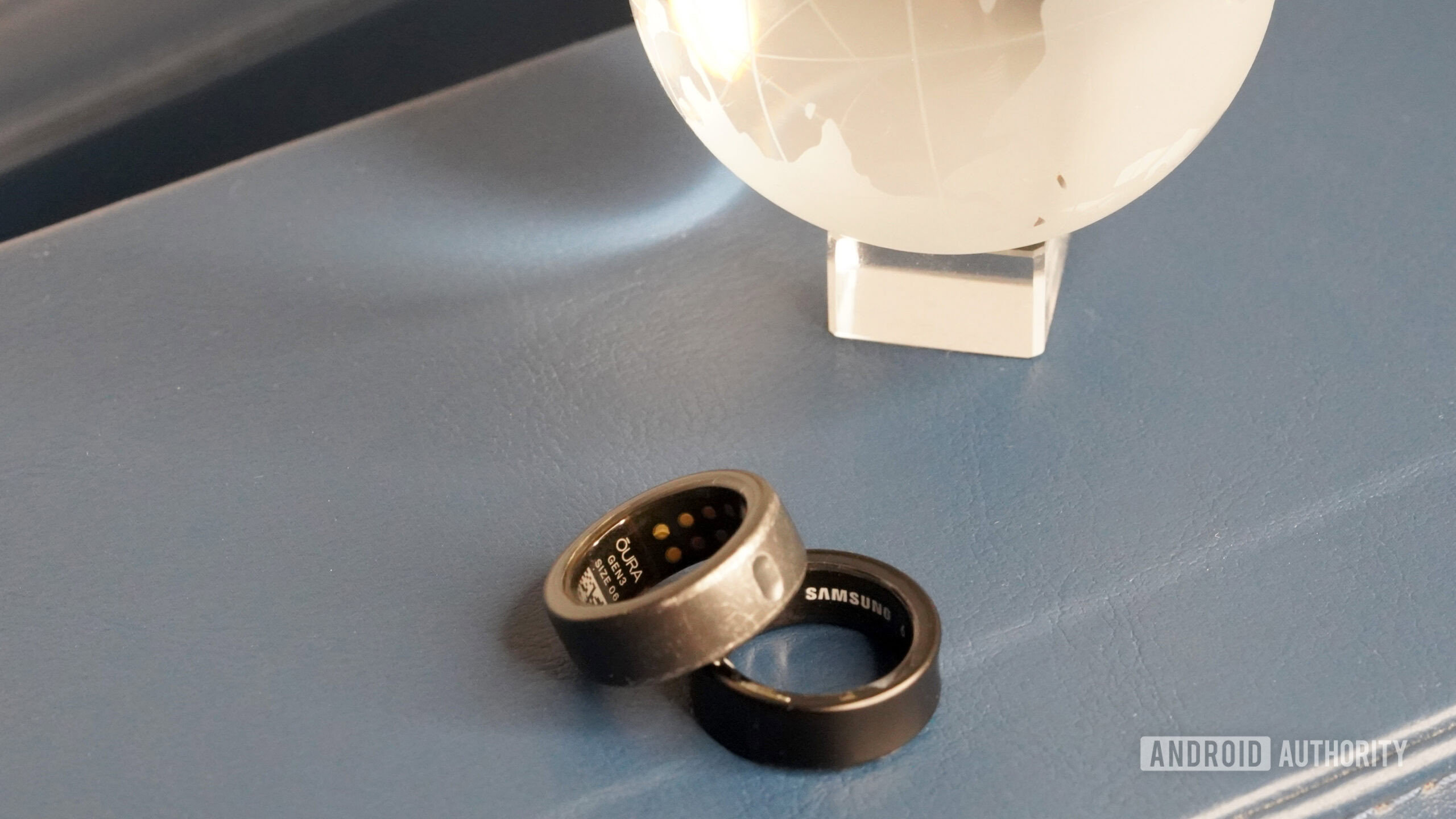 Samsung Galaxy Ring vs Oura Ring 3 Rótulos Um anel do Samsung Galaxy repousa ao lado de um ringue 3, cada um destacando o rótulo da sua empresa.