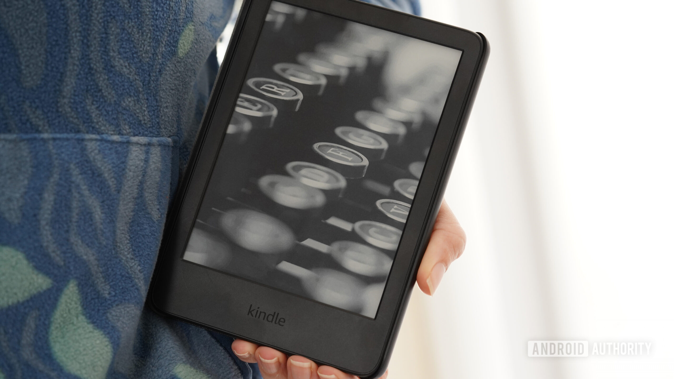 Protetor de tela Kindle 2024 Um usuário segura um Kindle 2024 contra um moletom estampado.