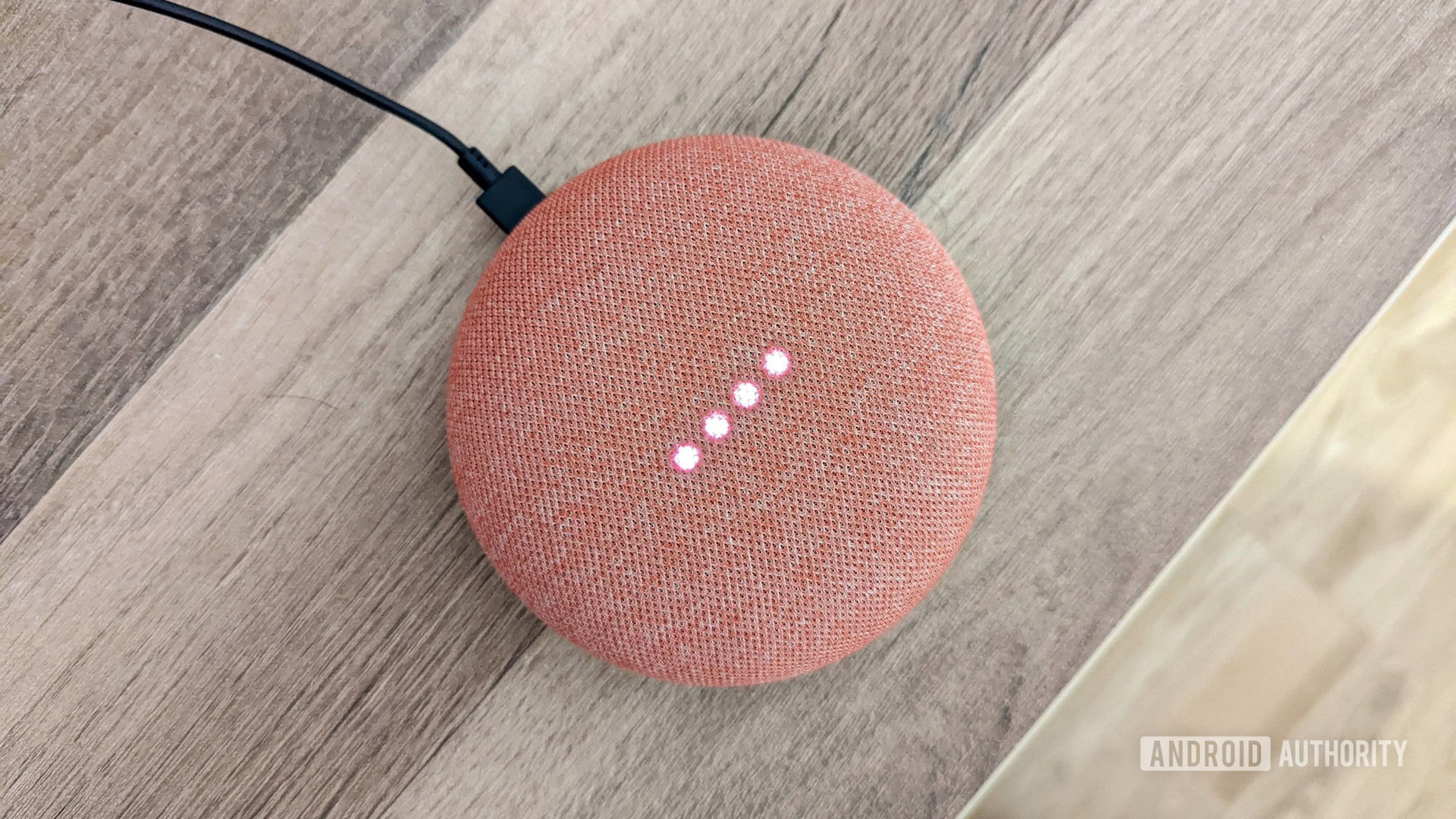Google Home Mini Luzes de coral acesas Google Home Mini em coral com luzes acesas, no fundo de madeira