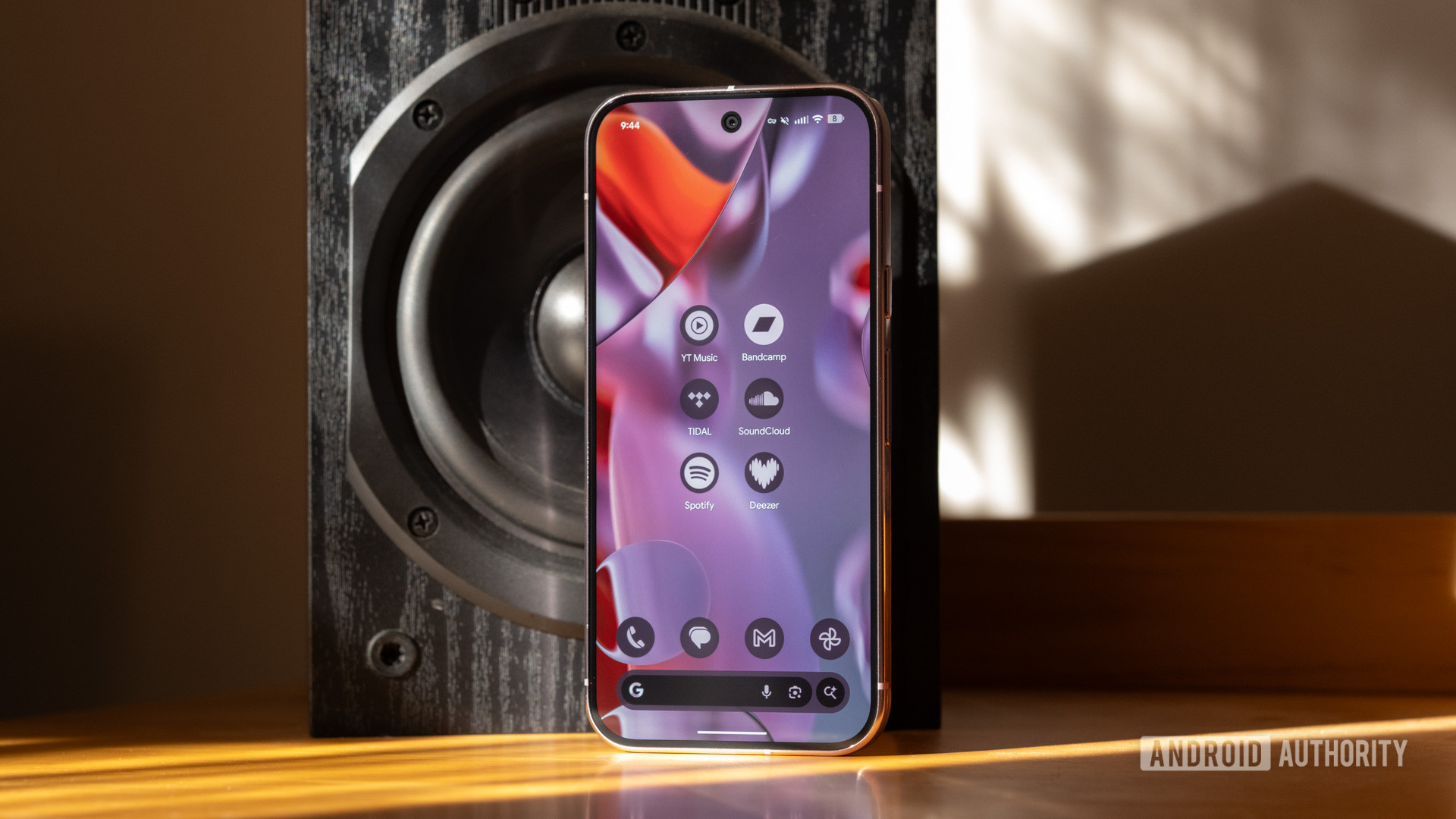 Google Pixel 9 Apps de streaming de música profissional Um Pixel 9 Pro ao lado de um alto -falante, exibindo vários ícones de aplicativos de streaming de música.