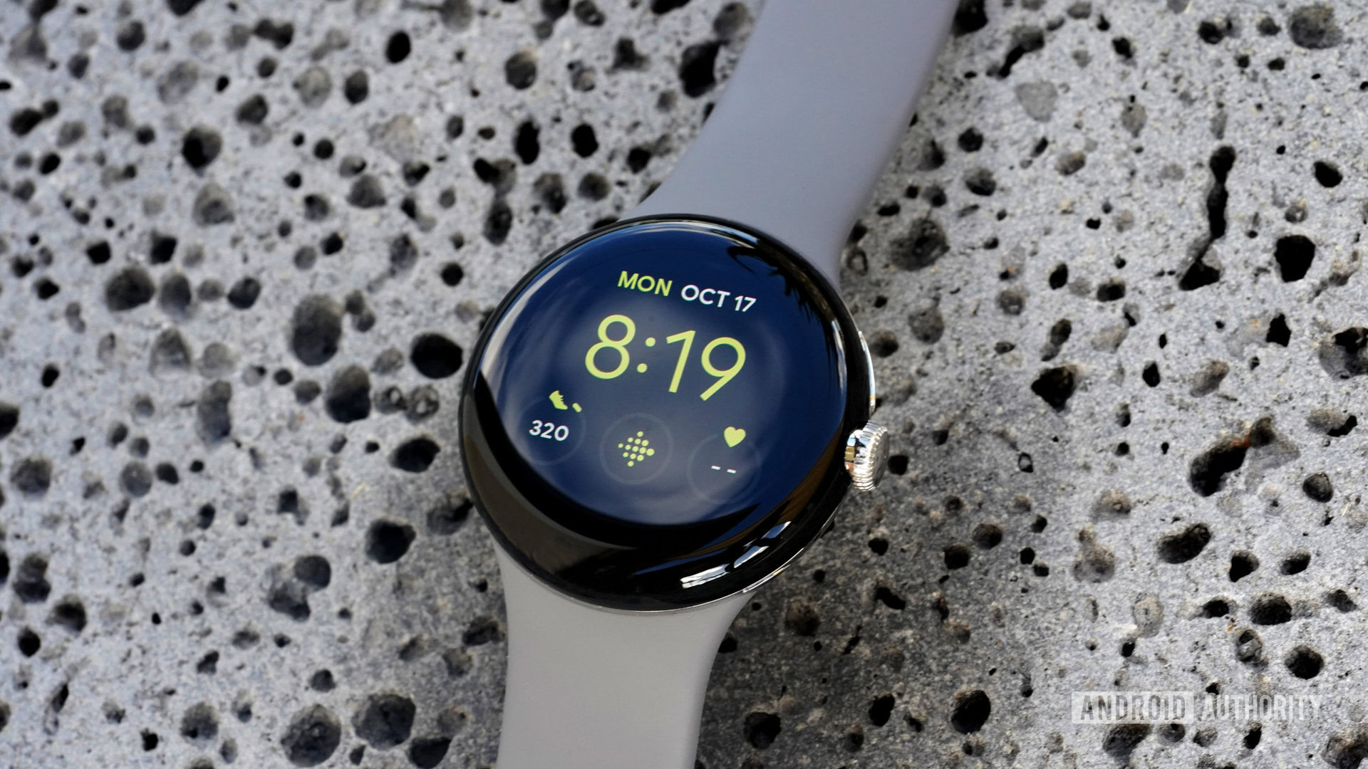 Mostrador do utilitário Google Pixel Watch Um Google Pixel Watch repousa sobre uma rocha de lava exibindo o mostrador do relógio Utility com um atalho do Fitbit.