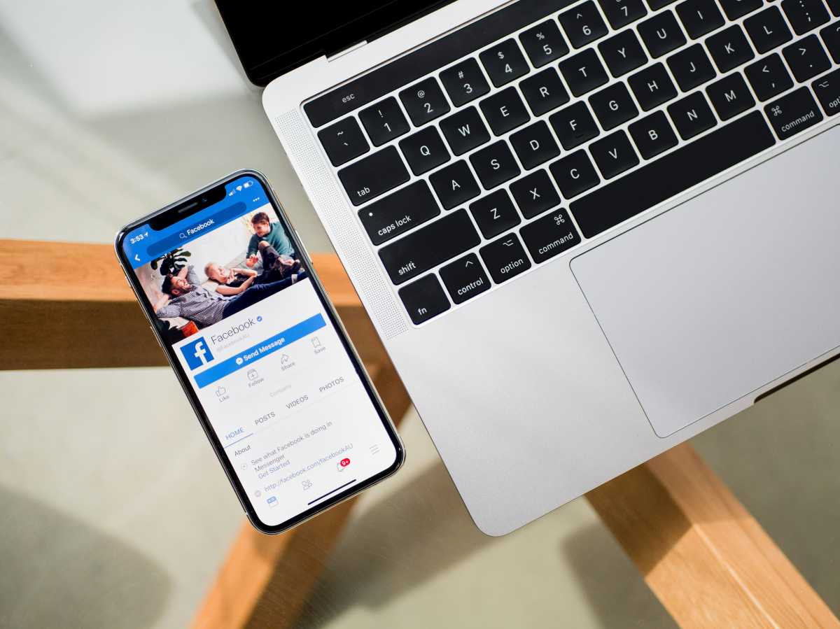Facebook em um smartphone próximo a um MacBook
