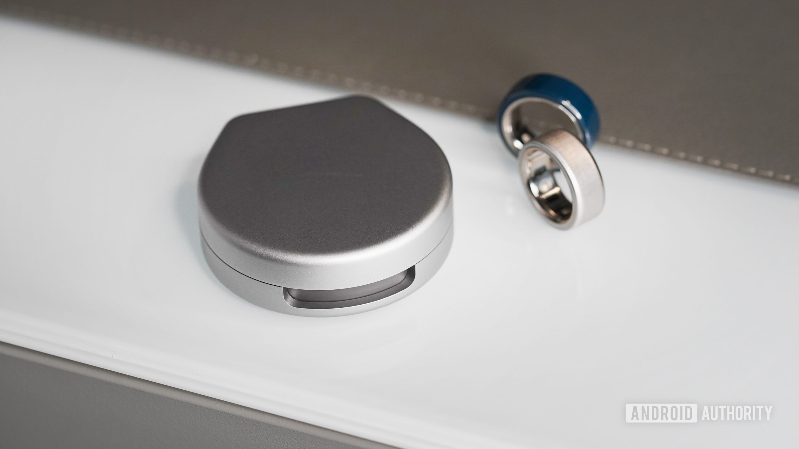 Carregador Oura Ring 4 Anéis Dois Oura Ring 4s ficam ao lado do estojo de carregamento portátil da marca.