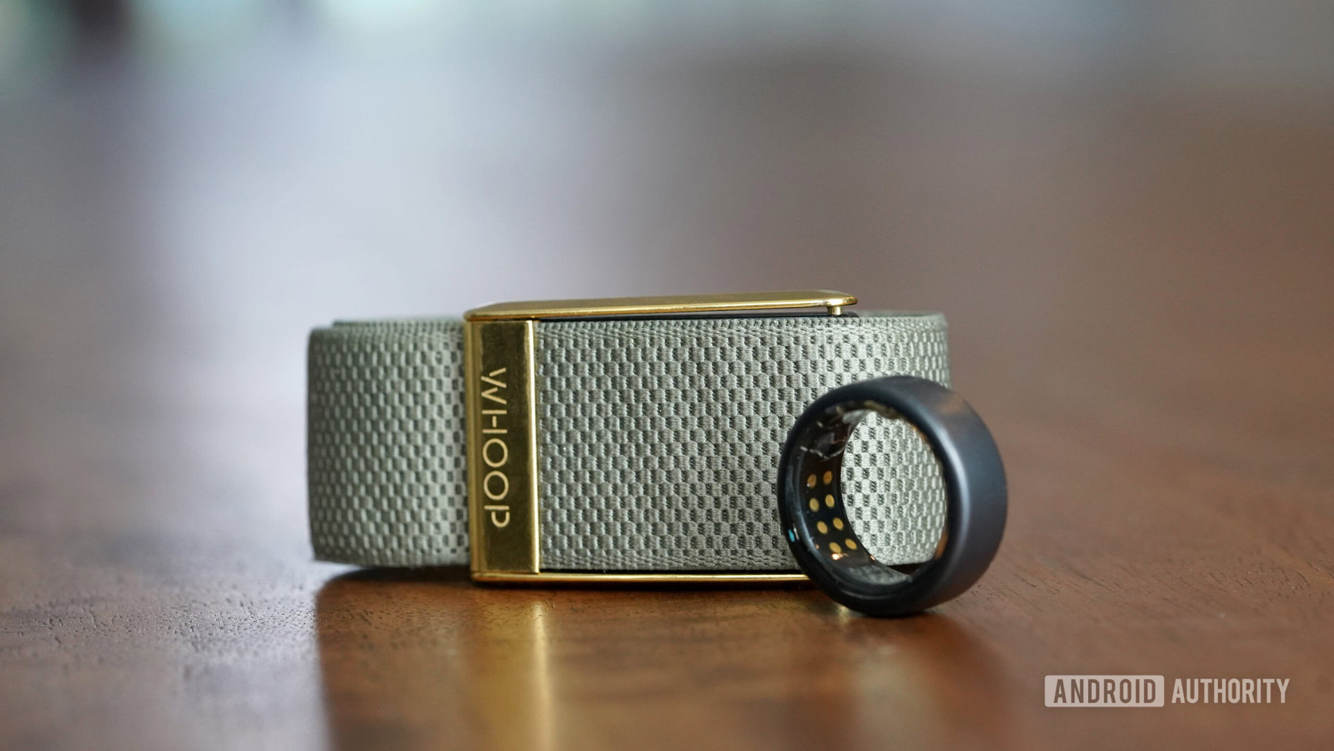 Um Oura Ring 3 e Whoop 4 ficam lado a lado em uma superfície de madeira.