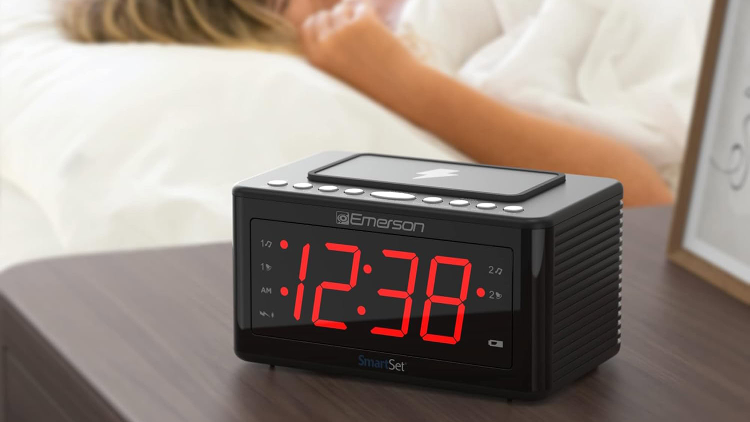 Rádio despertador de carregamento sem fio Emerson Smartset ao lado da cama e pessoa dormindo